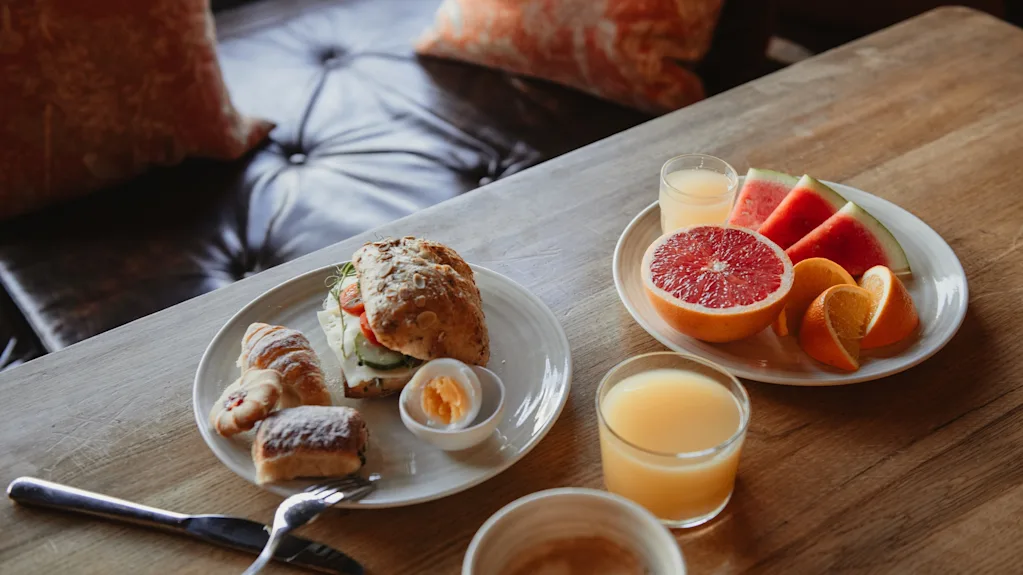 En utsökt frukostbuffé med en smörgås, bakverk, frukt och juice på ett träbord på Home Hotel Grand, Helsingborg.