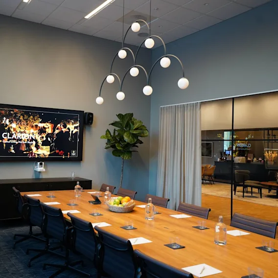A long conference table with chairs, set with notepads and water bottles, faces a large screen displaying "CLARION". A flipchart stands nearby in a modern meeting room.