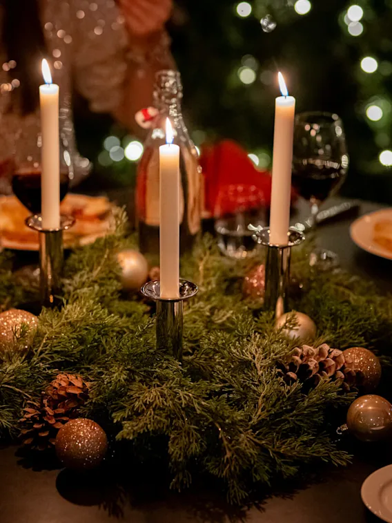 En festlig dukning med tända ljus, vinglas och en julgirlang som mittpunkt.