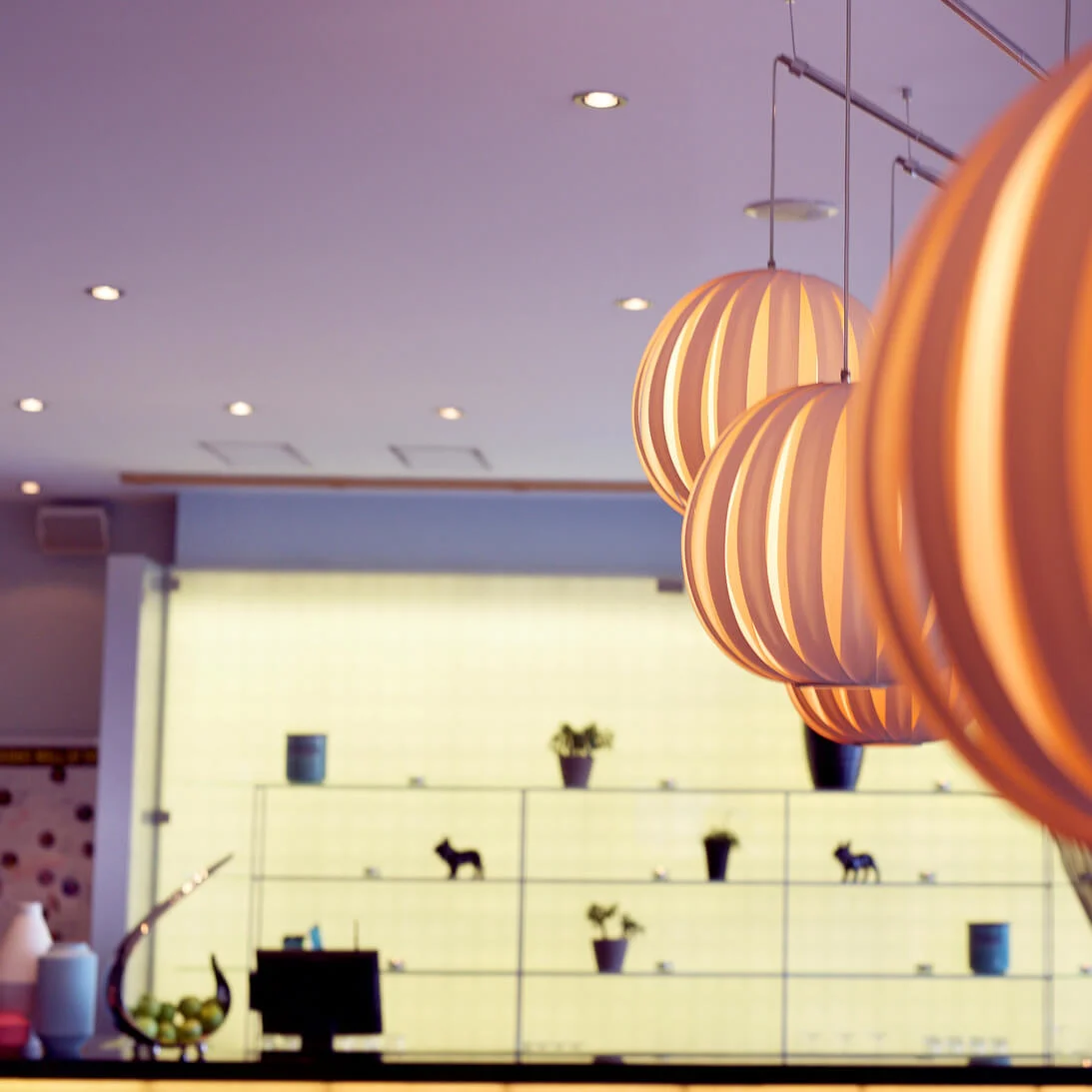 Modern pendant lights dominate the foreground of a softly lit, stylish interior space.