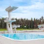 Suuri ulkouima-allas, jossa on useita uimahyppyalustoja, ympäröity korkealla metsällä pilvisen taivaan alla. Taustalla näkyy pieni rakennus.