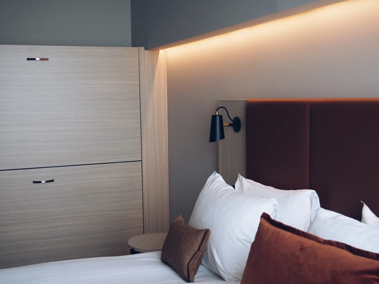 Et moderne hotellrom med en pent oppredd seng, myke puter, en stilig vegglampe og varm stemningsbelysning for et avslappende opphold.