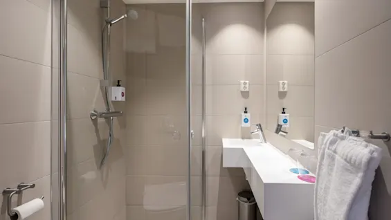 Et moderne og rent hotellbad med dusjnisje med glassdør, en elegant vask og et stort speil.