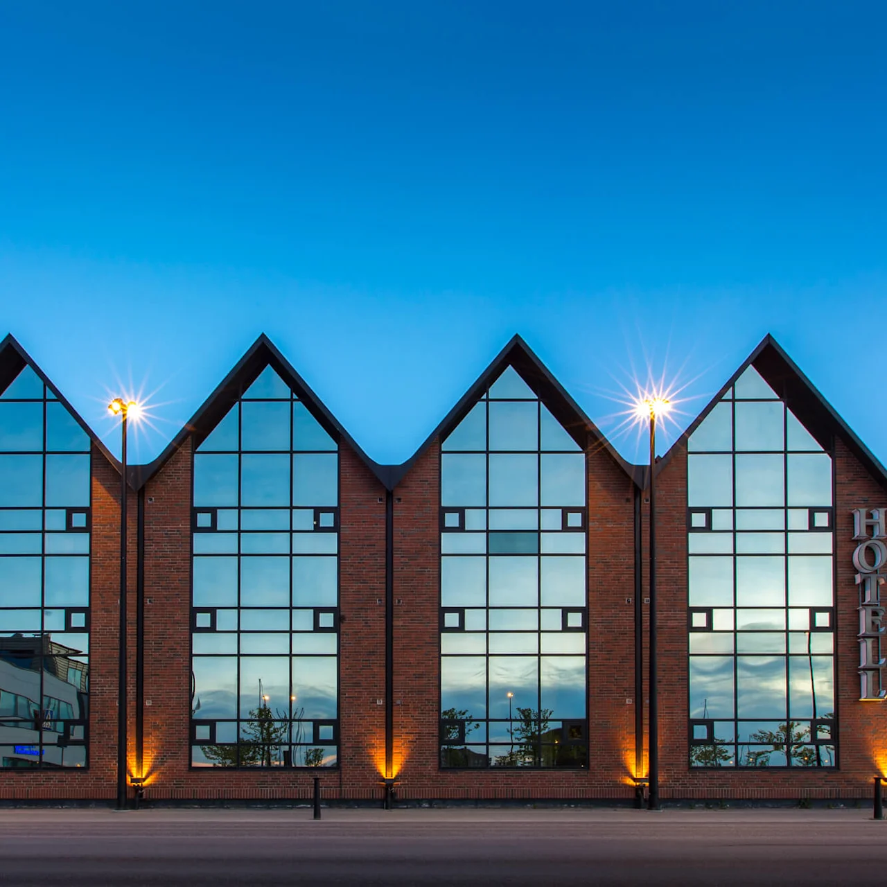 A modern hotel with large windows and triangular peaks at dusk, with lights illuminated and a clear blue sky.