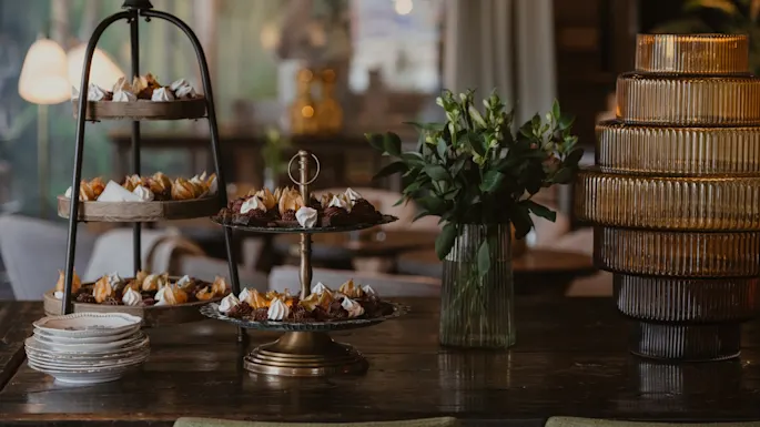 Et vakkert arrangert dessertbord med etasjefat fylt med småkaker, friskt løvverk og dekorative glasselementer.