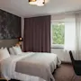 A serene hotel room with a comfortable bed, a dedicated workspace, and a window offering a peaceful view of nature.