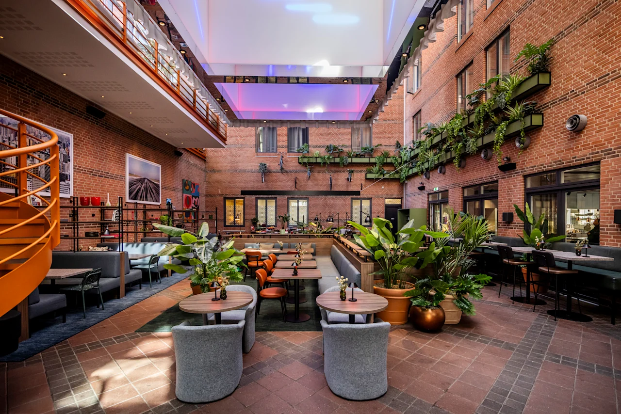 An inviting indoor courtyard at Comfort Hotel Vesterbro with dining tables, lush plants, and brick walls under a bright skylight.