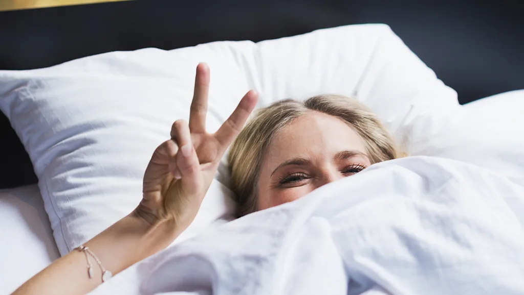 Woman in hotel bed showing the peace sign