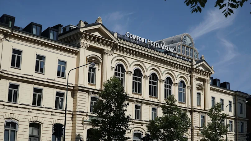 Classic facade of 'Comfort Hotel Malmö' with arched windows and a glass rooftop, against a clear sky.