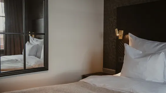 Ett mysigt hotellrum på Home Hotel Grand, Helsingborg, med en bekväm säng med vita lakan och en varm sänglampa.