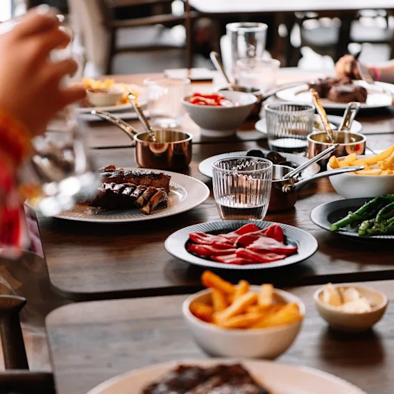 Ett bord dukat med utsökt mat, inklusive biff, pommes frites och grönsaker, för en social middagsupplevelse.