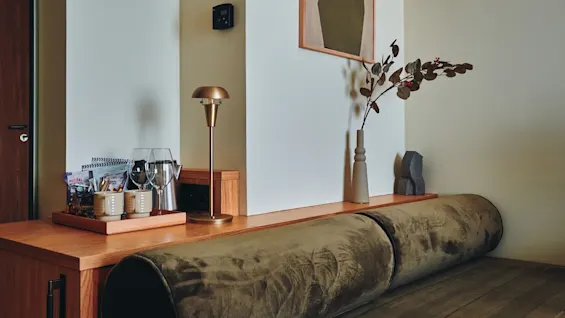 Et koselig hotellrom med en komfortabel dagseng, et sidebord i tre og abstrakt kunst på veggen, som skaper en avslappende atmosfære.