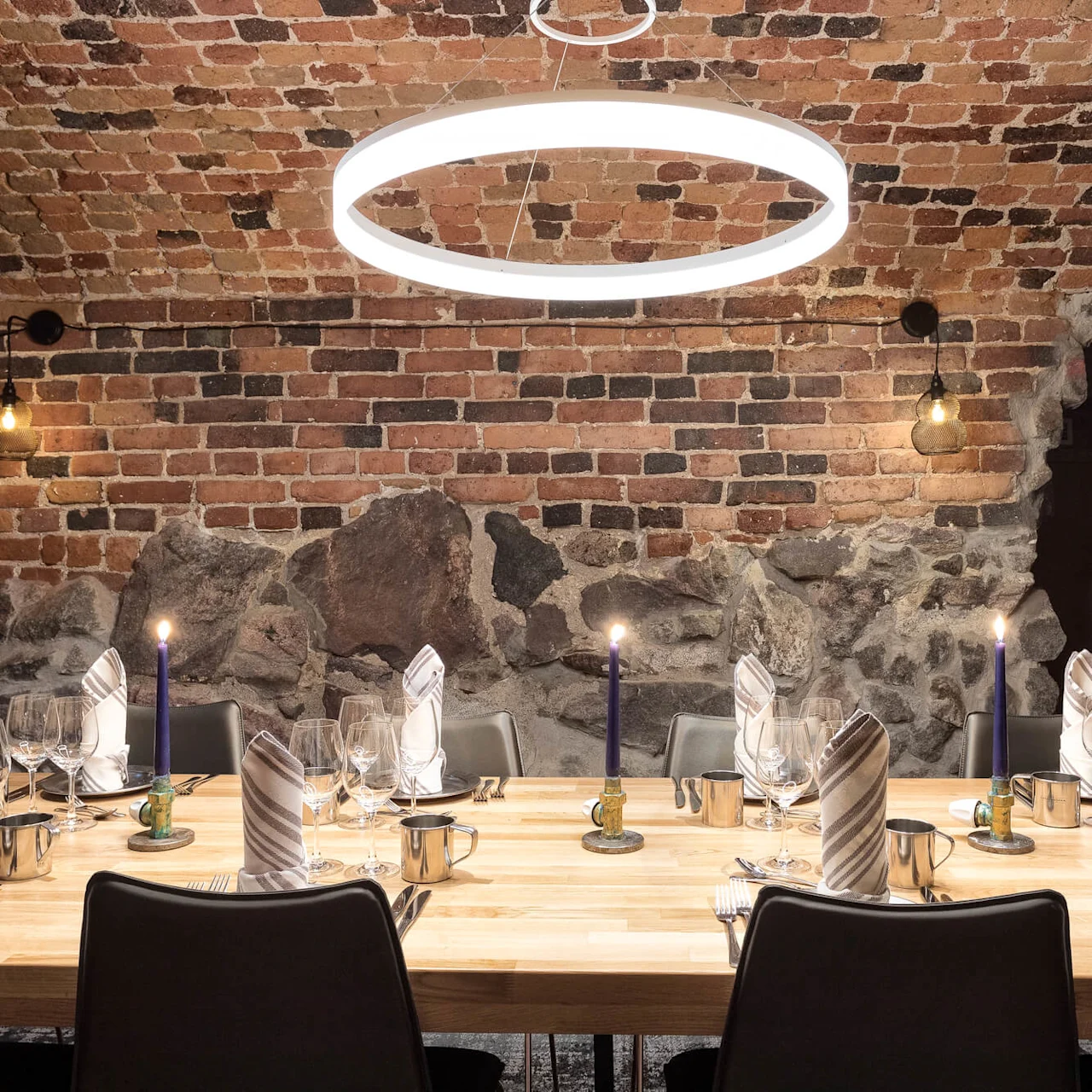 A set table with candles inside a room with brick walls and a hanging circular light.