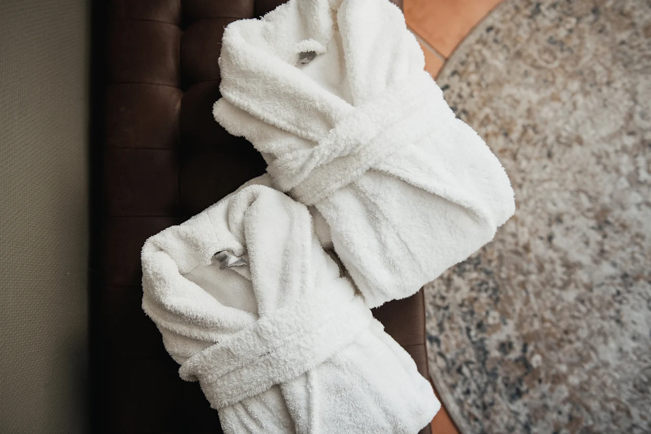Två mjuka vita badrockar prydligt vikta, inbjuder till komfort och avkoppling i en mysig miljö.