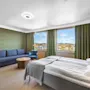 Lyst hotellrom med dobbeltseng, sofa og vinduer med utsikt.