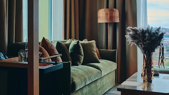 Et innbydende oppholdsrom med en plysjgrønn sofa, stilig belysning og varm innredning, perfekt for å slappe av.