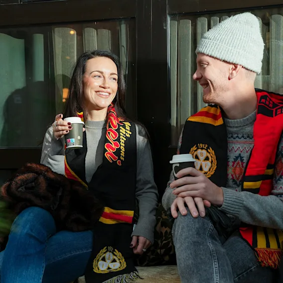 Två leende sportfans som sitter utomhus i vinterkläder och njuter av varm dryck tillsammans.