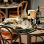 Ett runt matbord har tallrikar med gourmetmat, vinglas och en flaska, omgiven av trästolar i en varmt upplyst restaurangmiljö.