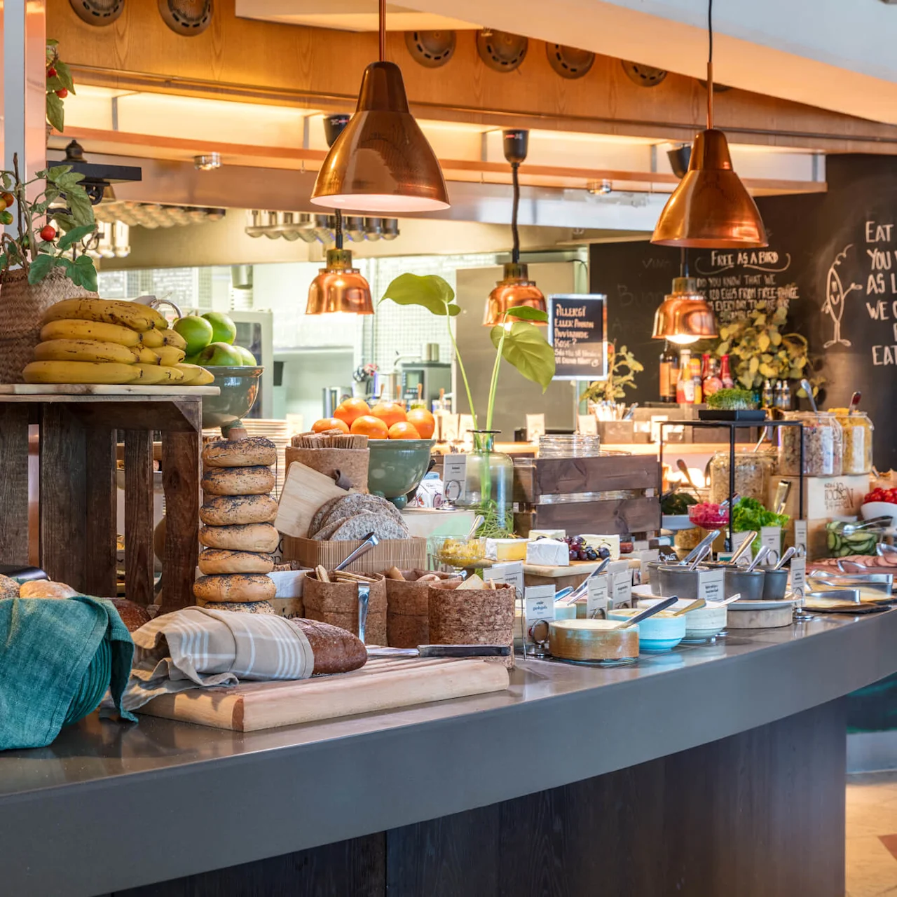Assorted fresh food displayed on a buffet with a chalkboard message emphasizing sustainable eating, in a cozy, well-lit dining setting.