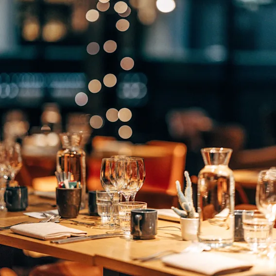 A beautifully set long table in a cozy restaurant with warm lighting and sparkling bokeh lights in the background.
