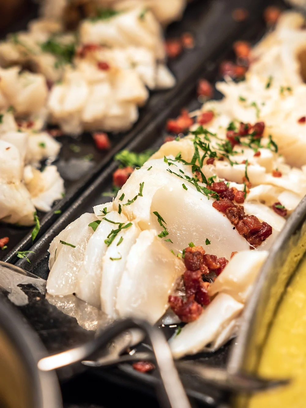 Skiver av kokt fisk toppet med urter og terninger av rødt tilbehør ligger på et fat. I nærheten gir en kremet gul rett fargekontrast til matpresentasjonen.