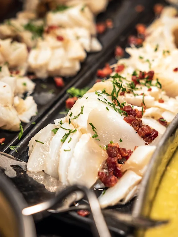 Skiver av kokt fisk toppet med urter og terninger av rødt tilbehør ligger på et fat. I nærheten gir en kremet gul rett fargekontrast til matpresentasjonen.