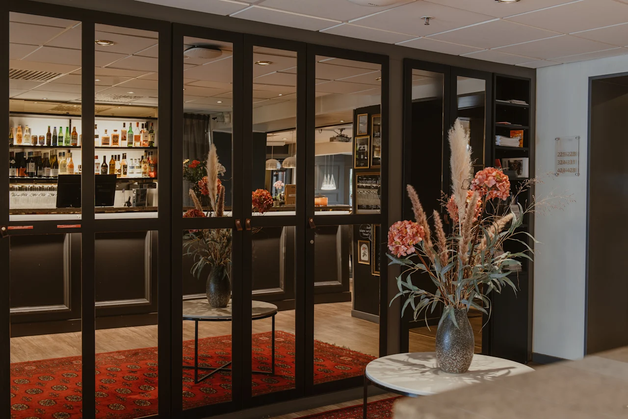 Home Hotel Kung Oscar bar area with glass doors reflecting bottles, flowers, and a red rug. Room numbers 225-238, 334-337, 433-435 are visible.