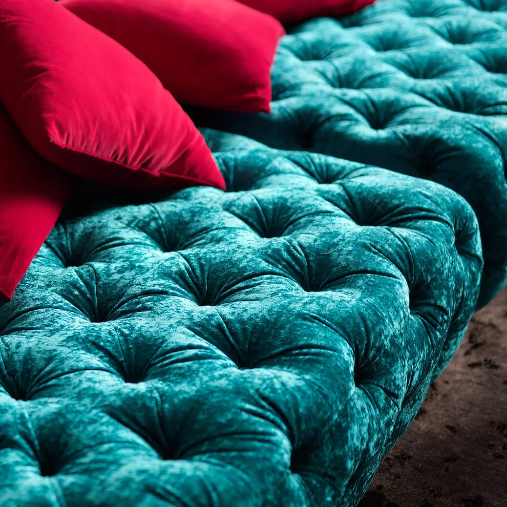 Turquoise velvet tufted sofa adorned with several red pillows, creating a striking color contrast in a cozy living room setting.