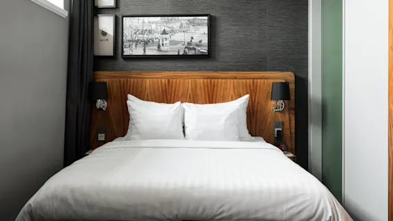 A neatly made bed with white linens in a room with dark grey walls and a black-and-white photo above it.