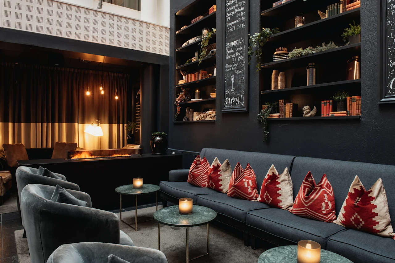 Et hyggeligt loungeområde med pejs, komfortable siddepladser og hylder fyldt med bøger. En menutavle læser: BUBBEL Enjoy!