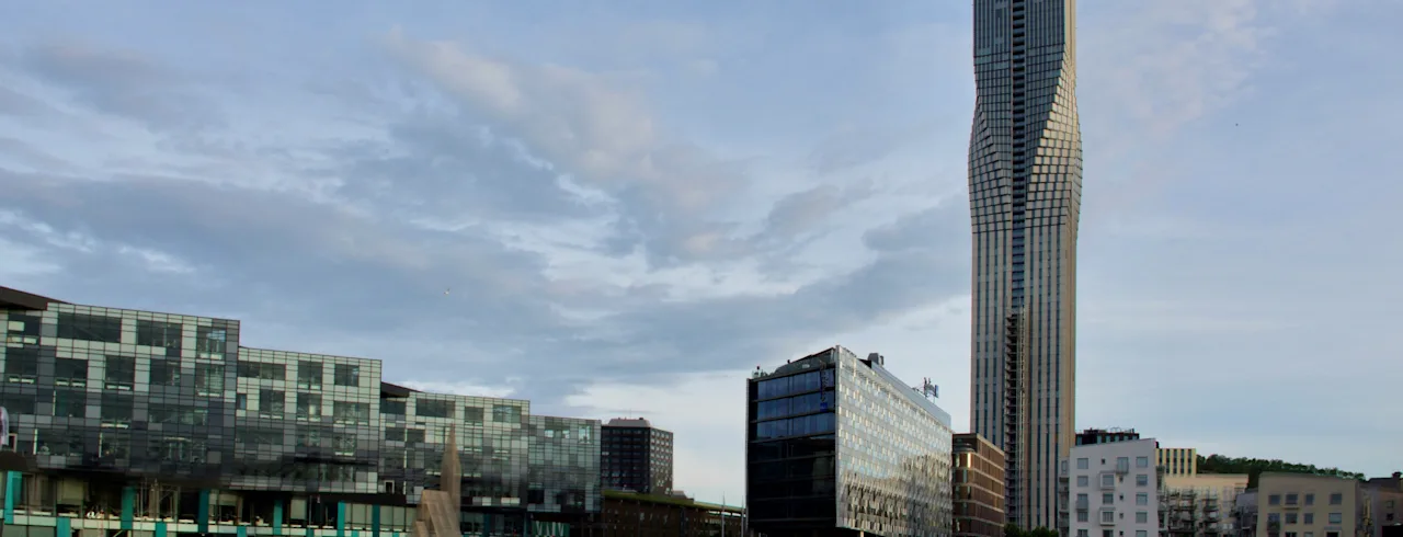 Et moderne bylandskap i Gøteborg med en høy, vridd skyskraper og bygninger speilet i vannet under en skyet himmel.