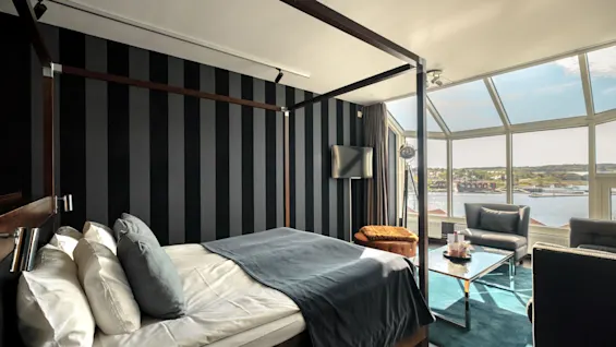 Et moderne hotelværelse med himmelseng, et hyggeligt siddeområde og store vinduer med naturskøn udsigt over vandet.