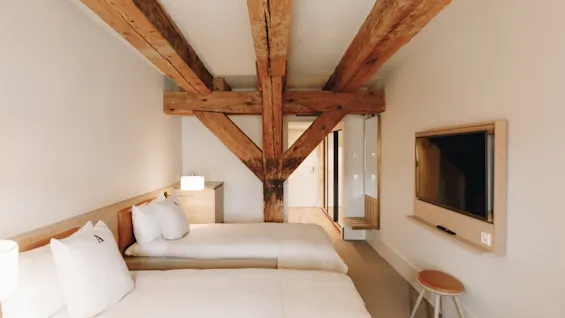 Ett mysigt hotellrum med två sängar, synliga takbjälkar i trä och en väggmonterad TV, som erbjuder en bekväm vistelse.