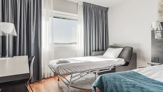 A cozy hotel room featuring a main bed and a convenient pull-out bed, bathed in natural light from the window.