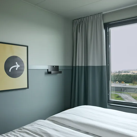 Ett mysigt rum på Stopover Hotel Falkenberg med en bekväm säng, ett fönster med utsikt och en unik väggkonst.