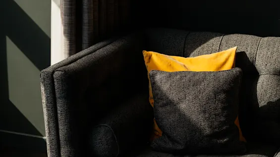 En hyggelig sofa med gule og grå puder, badet i sollys og skygger fra et nærliggende vindue.