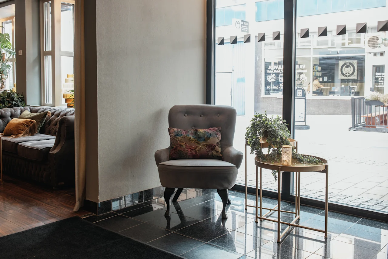 En bekväm hotellounge med en fåtölj och soffa, med utsikt över en gata med en reparationsverkstad.