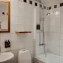 Et lyst og funksjonelt hotellbad med hvite fliser, vask, toalett og en dusj-badekar-kombinasjon.