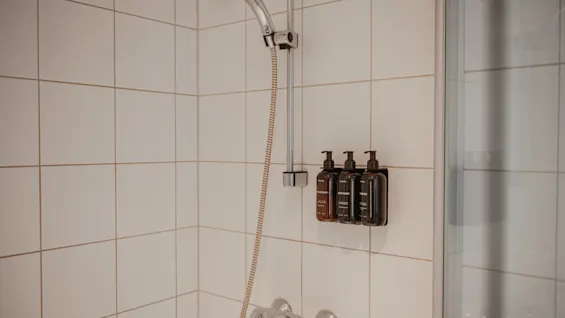 Ett rent och modernt duschutrymme med väggmonterade dispensrar för balsam, kroppstvål och schampo, redo att användas.