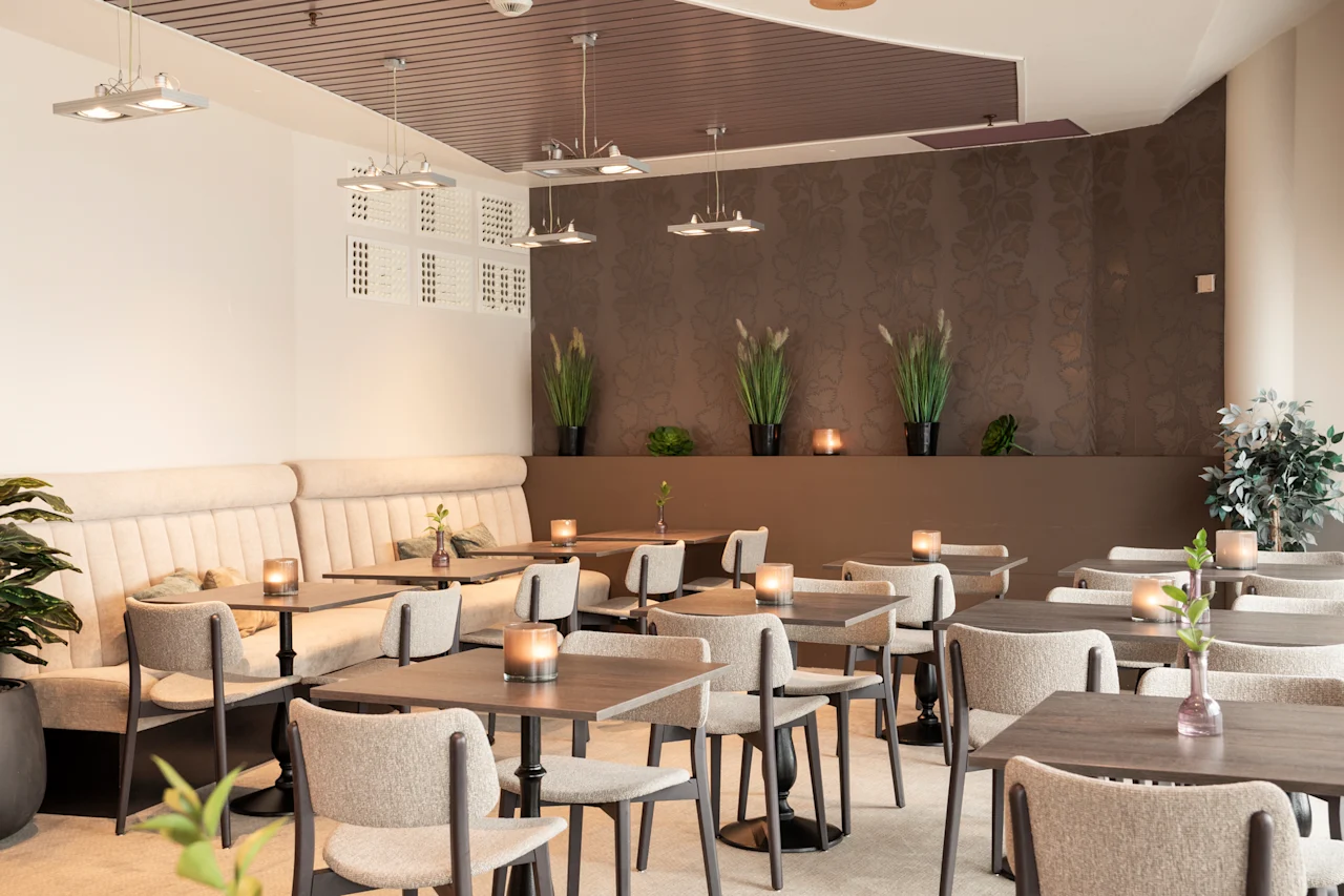 Viihtyisä ravintolaruokailutila, jossa on paljon pöytiä kynttilöineen, valmiina vieraille.