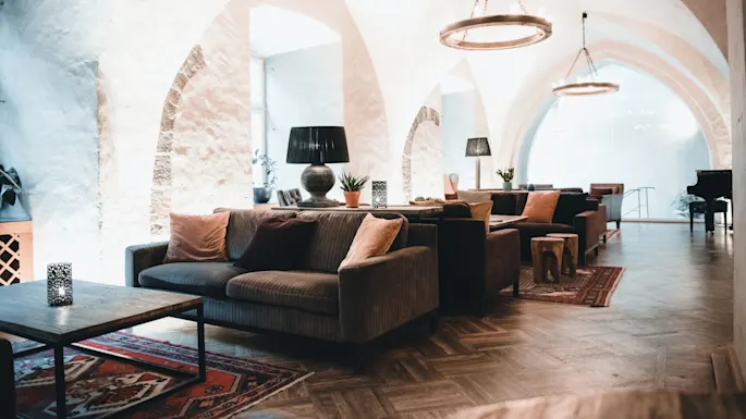 Hyggelig sittegruppe med sofaer og puter, med trebord og dekorative lamper, under hvelvede tak. Planter og et piano forbedrer den elegante, rolige atmosfæren.