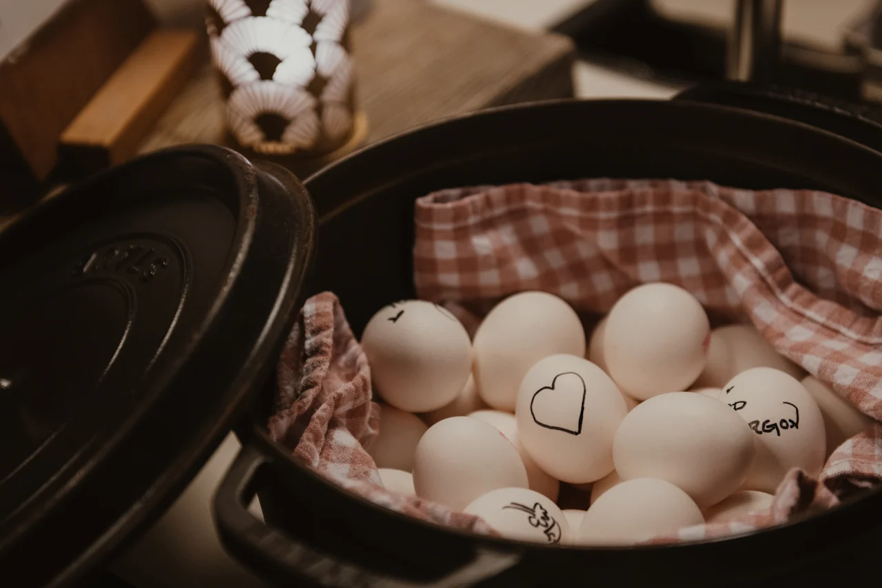 En gryde fyldt med hvide æg, nogle dekoreret med et hjerte og ordet region, indlejret i et ternet klæde. En lysestage er i baggrunden.