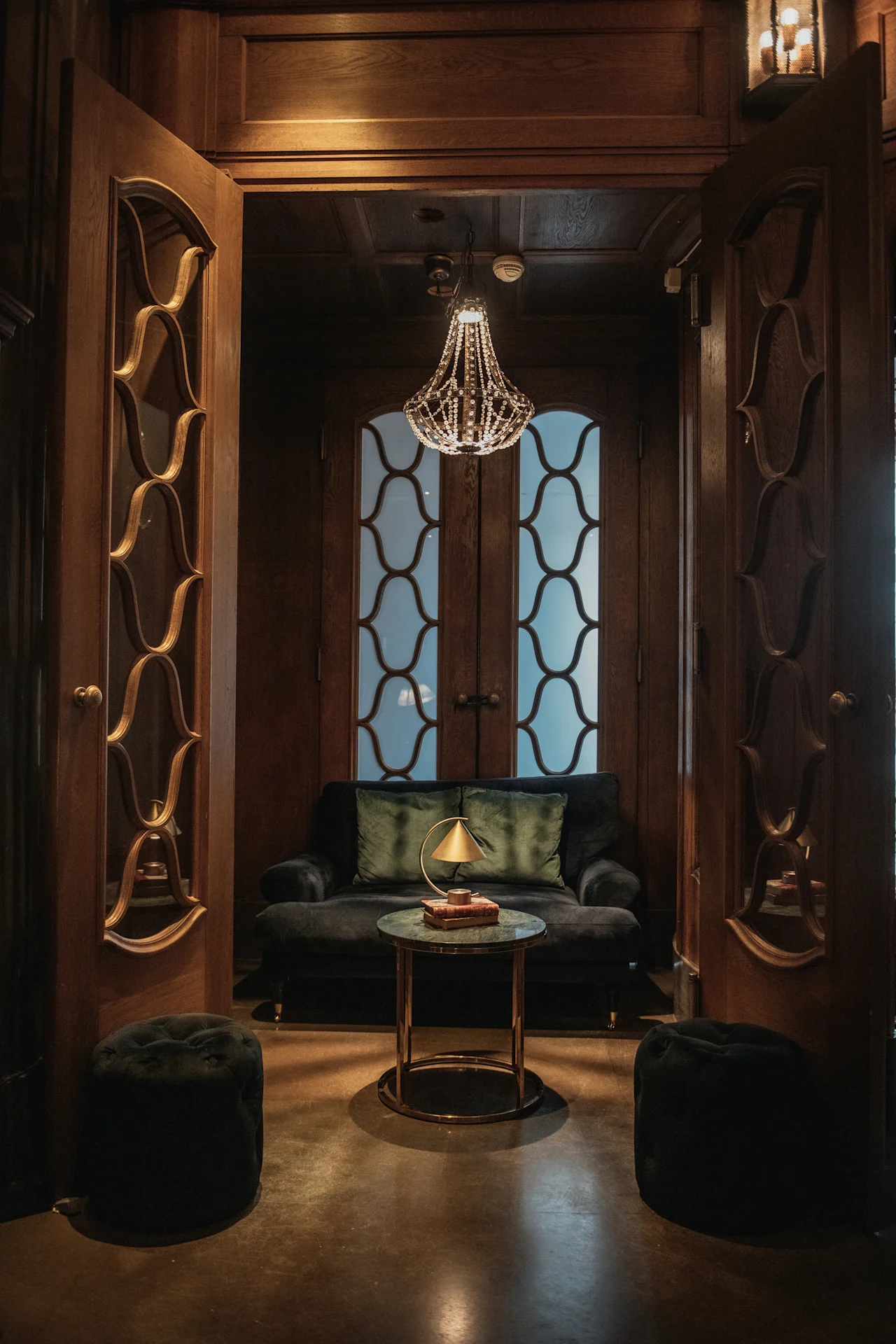 En lyxig och inbjudande lounge med mörka träpaneler, en bekväm soffa och ett litet bord med en lampa. Home Hotel Grand, Helsingborg.