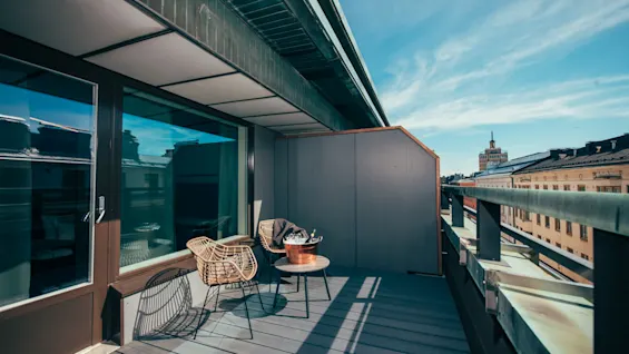 A sunny hotel balcony with outdoor seating and a city view, perfect for relaxing with a drink.