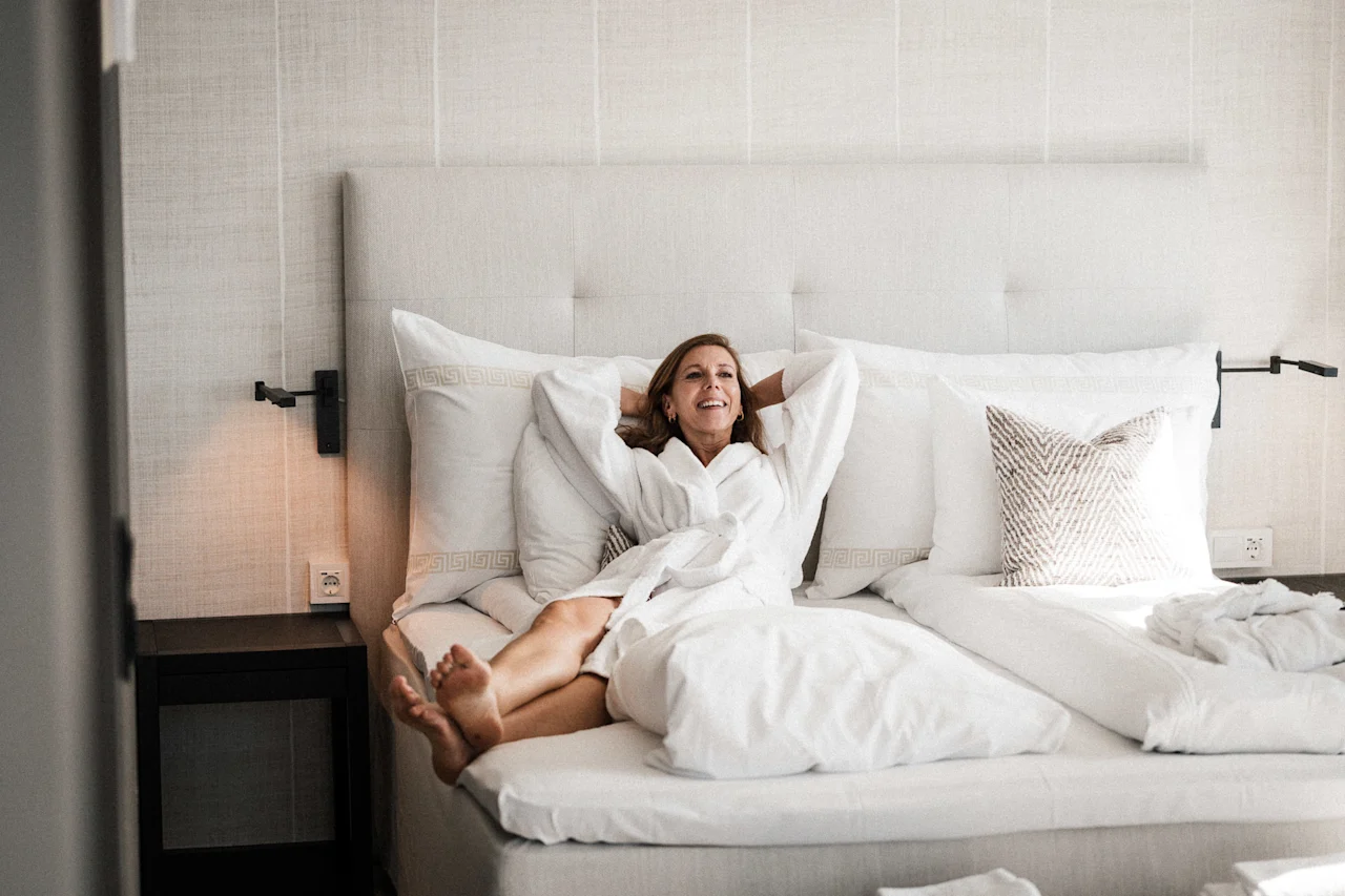 En person i hvit badekåpe slapper lykkelig av i en komfortabel seng.