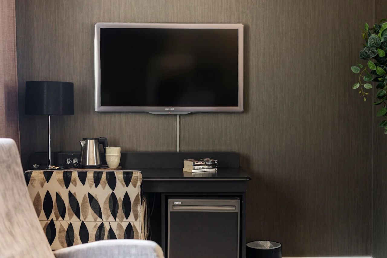 En bekväm hotellrumsinredning med en väggmonterad TV, en förfriskningsstation och en mysig sittplats.