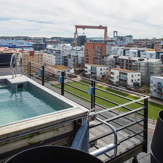 En takpool med metallstege med utsikt över stadsbilden inklusive bostadshus, en grön park och en stor kran märkt "ERIKSBERG". En färja med texten "Stena Line" synlig i bakgrunden.