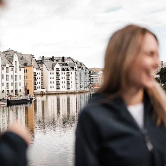 A person smiling by the water in front of the beautiful Art Nouveau buildings in Ålesund, Norway.