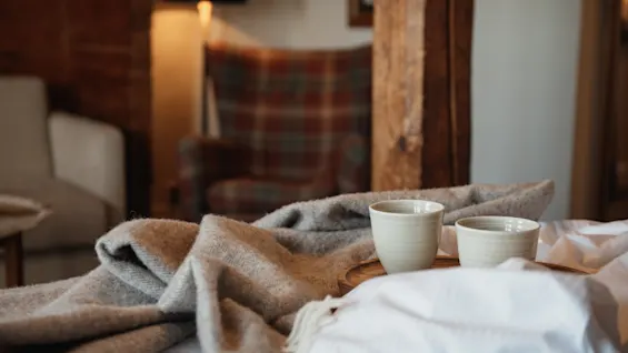 To varme drikke på en bakke ved siden af et hyggeligt tæppe, hvilket antyder et afslappende øjeblik i et behageligt rum.