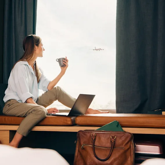 Woman looking out of hotel room with airplane in the background